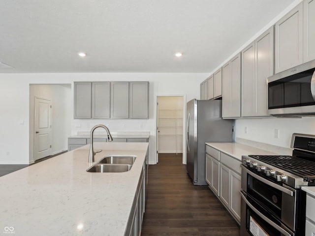 kitchen featuring appliances with stainless steel finishes, a sink, gray cabinetry, and light stone countertops