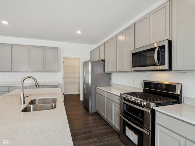 kitchen featuring appliances with stainless steel finishes, dark wood-type flooring, light stone countertops, gray cabinets, and a sink