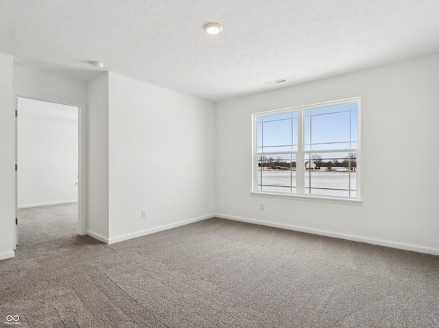 carpeted spare room featuring visible vents, baseboards, and a textured ceiling