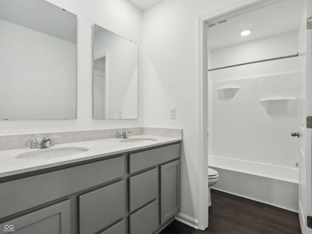 bathroom featuring toilet, double vanity, a sink, and wood finished floors