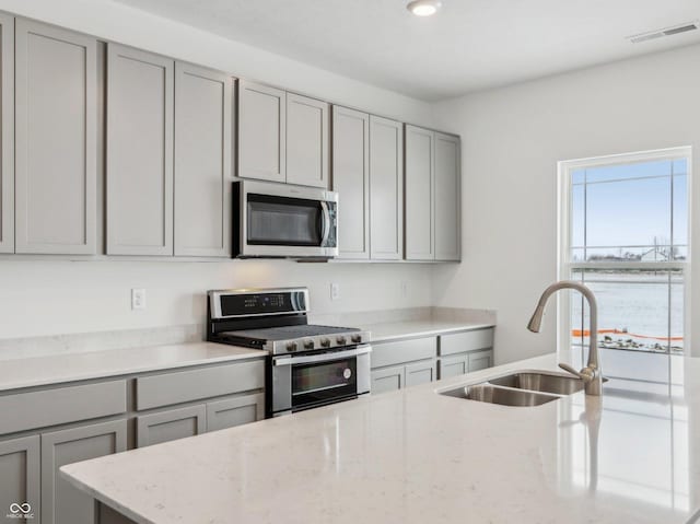 kitchen featuring light stone counters, stainless steel appliances, a sink, visible vents, and gray cabinets