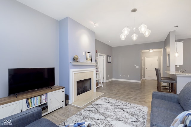 living room featuring an inviting chandelier, a tiled fireplace, and light wood-type flooring