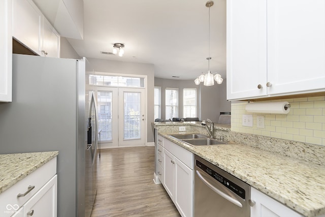 kitchen featuring appliances with stainless steel finishes, sink, pendant lighting, white cabinets, and light hardwood / wood-style flooring