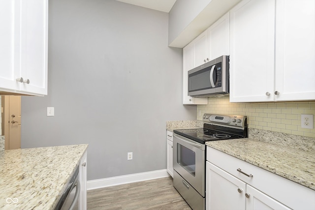 kitchen with light stone countertops, white cabinetry, light hardwood / wood-style floors, stainless steel appliances, and decorative backsplash