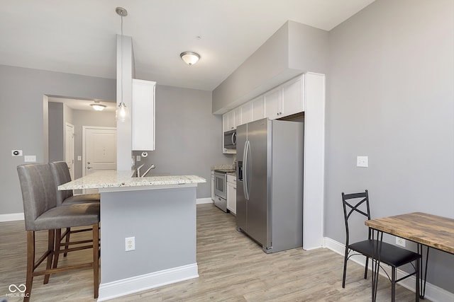 kitchen featuring kitchen peninsula, appliances with stainless steel finishes, white cabinetry, a kitchen bar, and light wood-type flooring