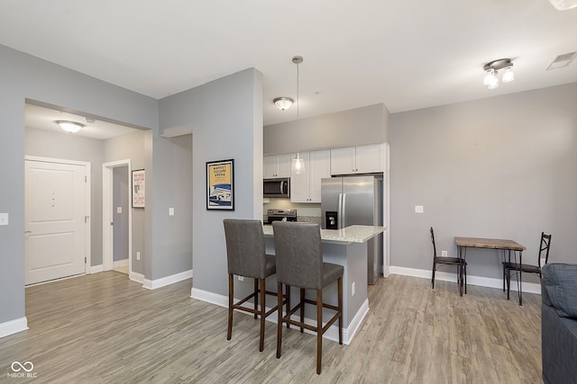 kitchen featuring light stone counters, white cabinetry, a kitchen bar, light hardwood / wood-style flooring, and stainless steel appliances