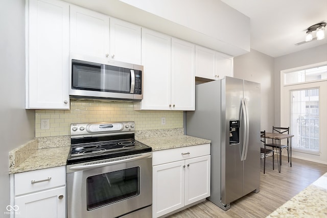 kitchen with appliances with stainless steel finishes, light hardwood / wood-style flooring, white cabinets, and tasteful backsplash