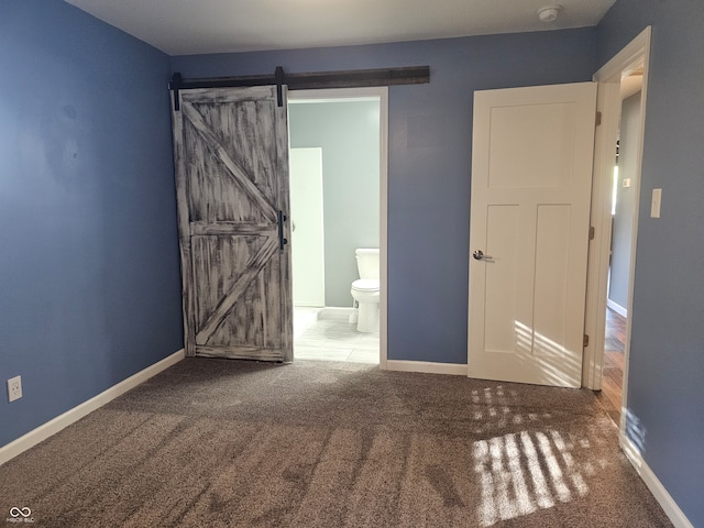 unfurnished bedroom with connected bathroom, a barn door, and carpet