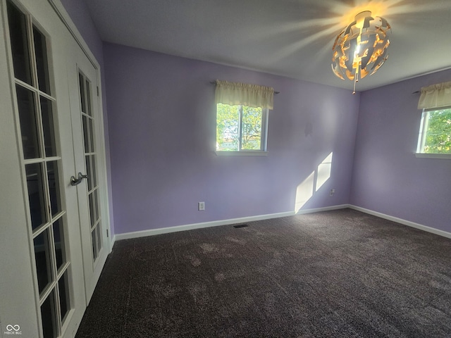 unfurnished room with a wealth of natural light, dark carpet, and french doors