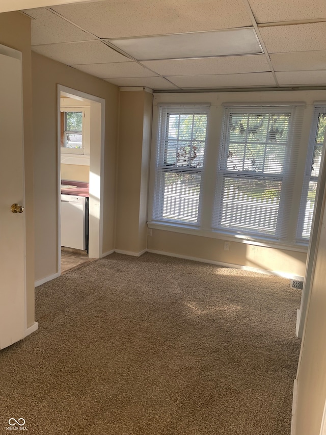 empty room with carpet floors, a paneled ceiling, and a healthy amount of sunlight