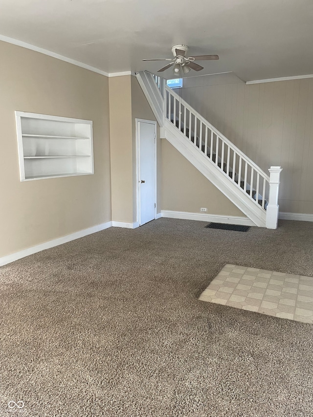 carpeted spare room featuring ceiling fan, wooden walls, crown molding, and built in shelves