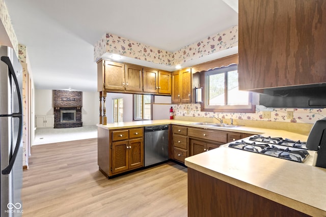 kitchen featuring stainless steel appliances, sink, kitchen peninsula, a brick fireplace, and light hardwood / wood-style flooring