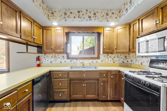 kitchen with light hardwood / wood-style floors, white range with gas stovetop, dishwashing machine, and sink