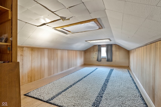 bonus room featuring vaulted ceiling and wood walls