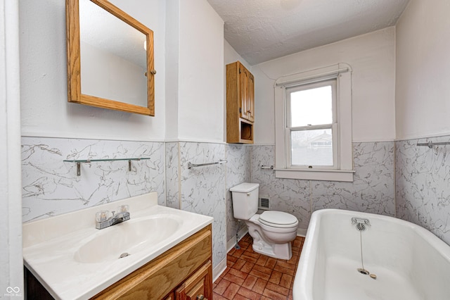 bathroom with a bathing tub, a textured ceiling, toilet, vanity, and tile walls