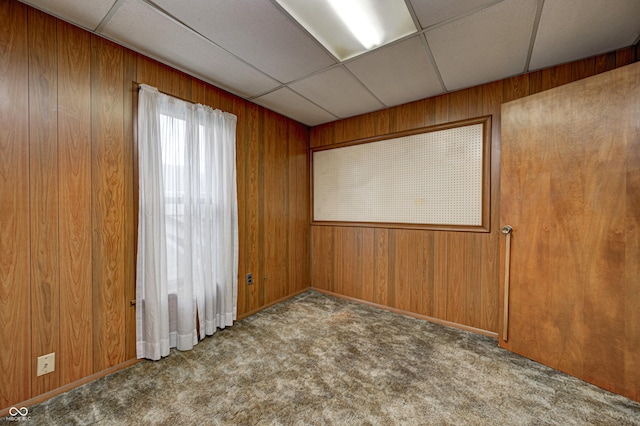 carpeted empty room featuring a drop ceiling and wooden walls