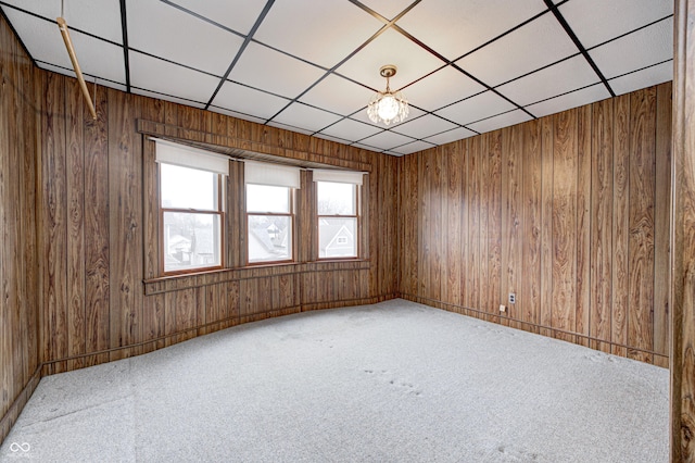 carpeted empty room featuring a drop ceiling and wood walls