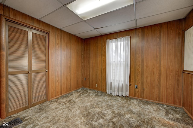 unfurnished room with a paneled ceiling, wooden walls, and light colored carpet