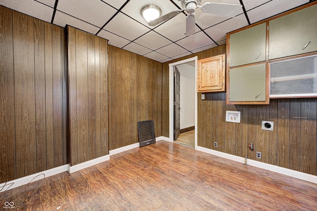 interior space with a drop ceiling, wood walls, ceiling fan, and light hardwood / wood-style flooring