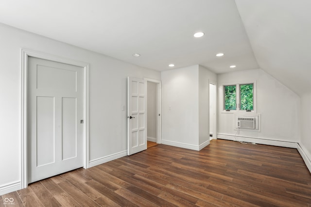 additional living space with a wall mounted air conditioner, vaulted ceiling, and dark hardwood / wood-style flooring