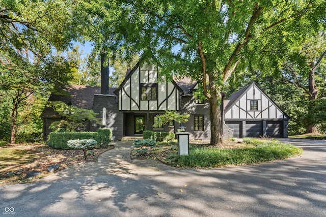 tudor-style house with aphalt driveway, roof with shingles, and stucco siding