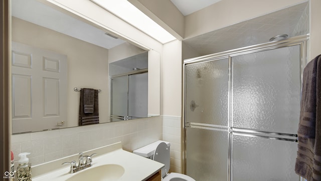 bathroom featuring vanity, a shower with door, toilet, and tile walls