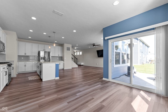 kitchen featuring white cabinetry, stainless steel appliances, decorative light fixtures, hardwood / wood-style flooring, and a kitchen island with sink