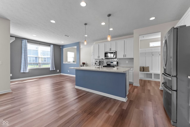 kitchen with a kitchen island with sink, dark wood-type flooring, decorative light fixtures, white cabinetry, and appliances with stainless steel finishes