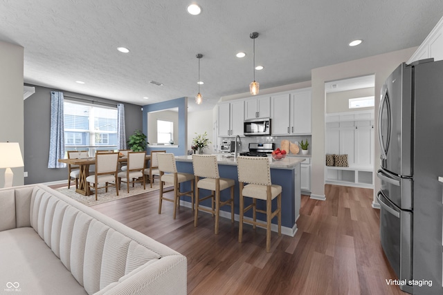 kitchen featuring an island with sink, white cabinetry, dark hardwood / wood-style floors, pendant lighting, and stainless steel appliances