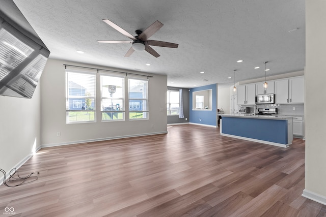 unfurnished living room with sink, a textured ceiling, and light hardwood / wood-style flooring