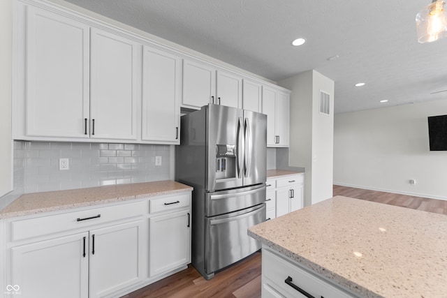 kitchen featuring light stone countertops, backsplash, stainless steel fridge, white cabinetry, and dark wood-type flooring