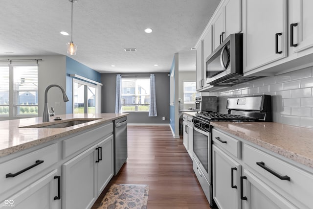 kitchen with dark wood-type flooring, sink, white cabinets, decorative light fixtures, and appliances with stainless steel finishes