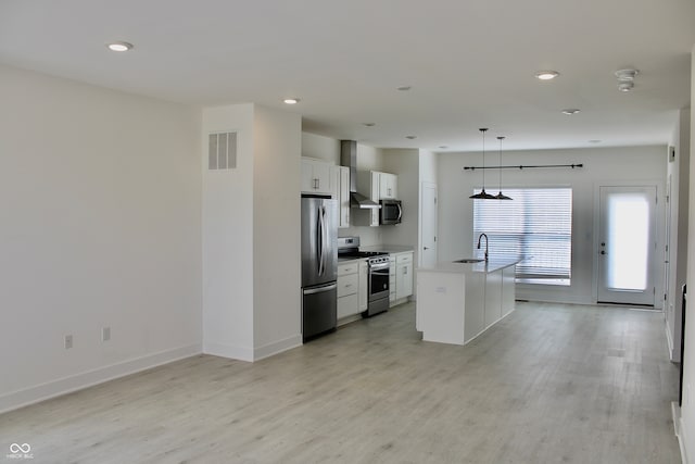 kitchen featuring light hardwood / wood-style floors, hanging light fixtures, appliances with stainless steel finishes, an island with sink, and white cabinetry