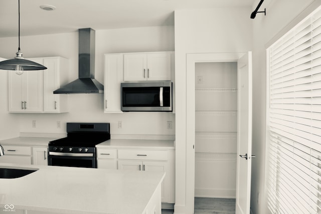 kitchen with white cabinets, appliances with stainless steel finishes, wall chimney exhaust hood, and pendant lighting