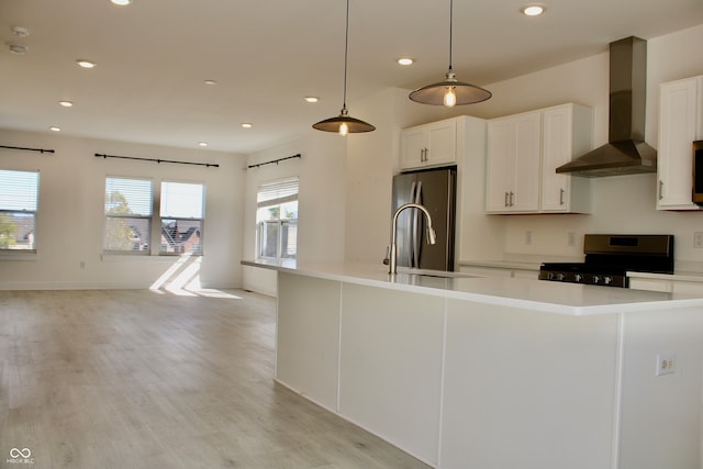 kitchen with white cabinets, stainless steel fridge, black range with gas cooktop, pendant lighting, and wall chimney range hood