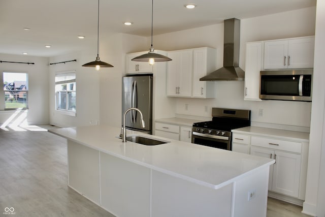 kitchen with wall chimney exhaust hood, a kitchen island with sink, sink, stainless steel appliances, and white cabinetry