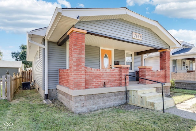 bungalow-style home featuring a porch, brick siding, central air condition unit, and fence