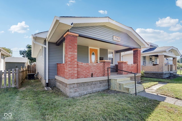 bungalow-style home featuring covered porch, a front yard, fence, and brick siding