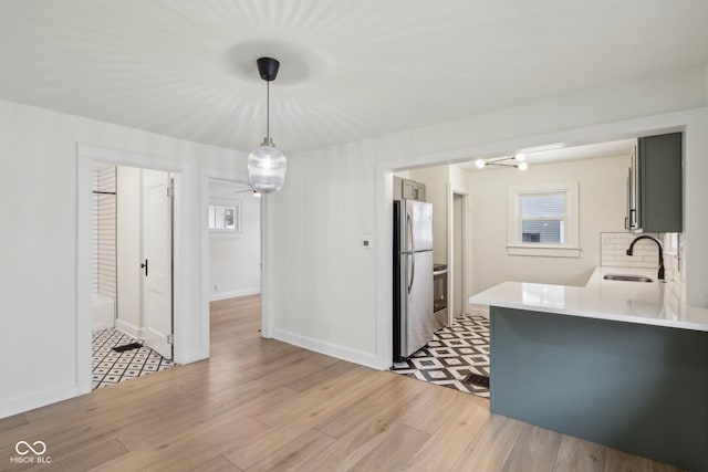 kitchen with decorative light fixtures, kitchen peninsula, sink, light wood-type flooring, and stainless steel fridge