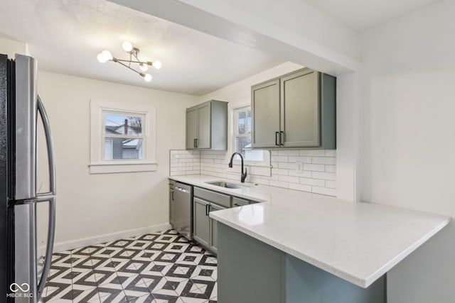 kitchen with kitchen peninsula, stainless steel appliances, tasteful backsplash, a chandelier, and sink