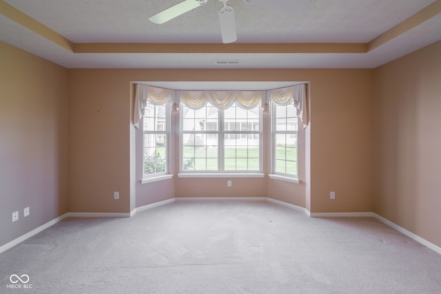 empty room featuring ceiling fan, light carpet, and a tray ceiling