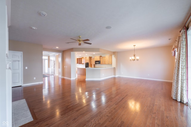 unfurnished living room featuring ceiling fan with notable chandelier and dark hardwood / wood-style flooring