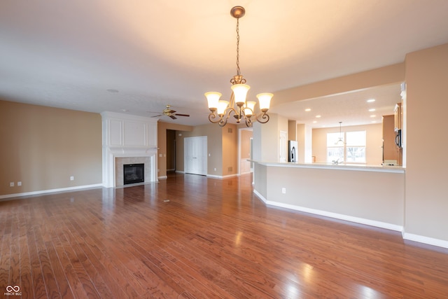 unfurnished living room with hardwood / wood-style flooring, ceiling fan with notable chandelier, and a fireplace