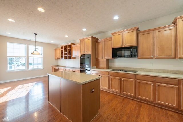 kitchen with a textured ceiling, black appliances, light hardwood / wood-style flooring, a kitchen island, and hanging light fixtures