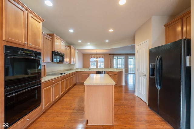 kitchen with a center island, kitchen peninsula, a chandelier, black appliances, and light wood-type flooring