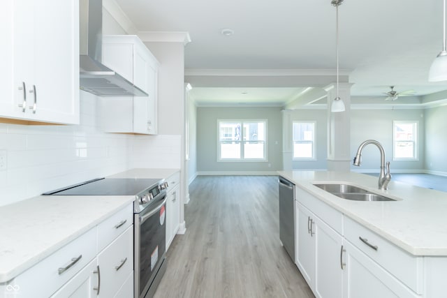 kitchen featuring appliances with stainless steel finishes, wall chimney exhaust hood, a healthy amount of sunlight, and decorative light fixtures