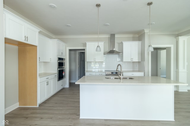 kitchen featuring wall chimney exhaust hood, an island with sink, and decorative light fixtures