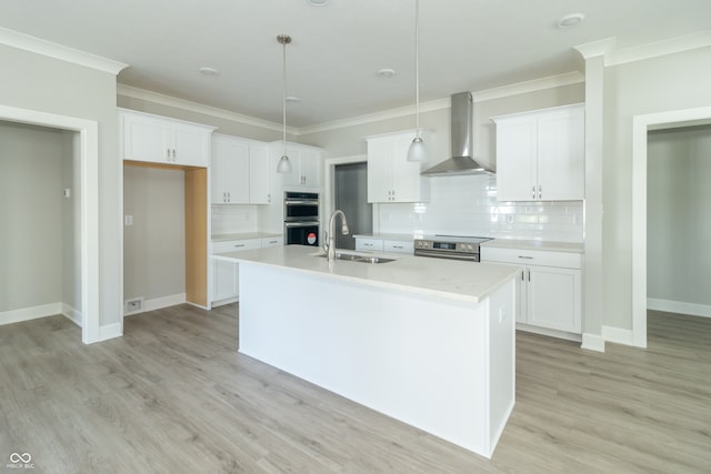 kitchen featuring sink, decorative light fixtures, white cabinetry, and wall chimney range hood