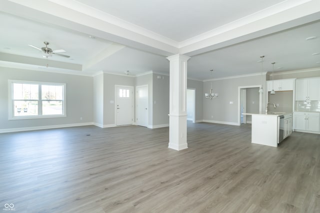 unfurnished living room with decorative columns, ceiling fan with notable chandelier, crown molding, sink, and wood-type flooring