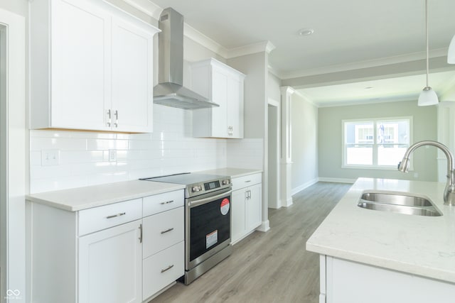 kitchen with stainless steel range with electric stovetop, wall chimney exhaust hood, sink, pendant lighting, and white cabinets